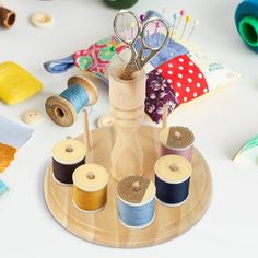 several spools of thread are sitting on a wooden tray with scissors and sewing needles