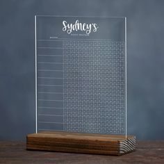 a clear acrylic desk calendar on top of a wooden stand with the word sydney written in cursive writing