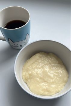 a bowl of batter next to a cup of coffee on a white counter top with a cat mug