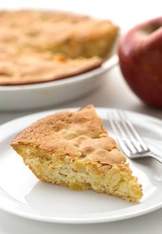 a piece of pie on a plate with an apple in the background and a fork next to it