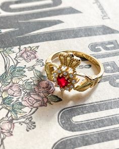 The Cezanna Ring is the perfect accessory for those seeking a touch of elegance and romance. Featuring a traditional Claddagh design adorned with a beautiful faux ruby heart and delicate pearls, this ring is sure to capture the heart of anyone who wears it. Add a touch of sophistication to any outfit with this stunning piece. Red Heart Ring With Center Stone For Wedding, Heirloom Heart Ring With Birthstone For Wedding, Classic Red Heart Ring For Wedding, Wedding Heart Ring With Ruby Center Stone, Wedding Heart-shaped Ruby Rings, Ruby Heart-shaped Wedding Birthstone Ring, Classic Ruby Heart Ring For Wedding, Classic Heart-shaped Birthstone Wedding Ring, Ruby Heart