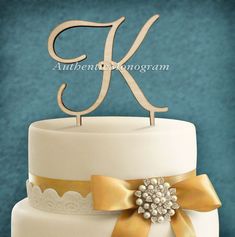 a white cake with gold ribbon and monogrammed letter k on top is shown