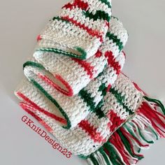 two white and red knitted scarves stacked on top of each other with green, red, and white fringes