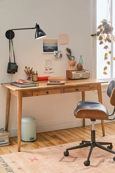 a desk with a chair, lamp and other items on it in front of a window