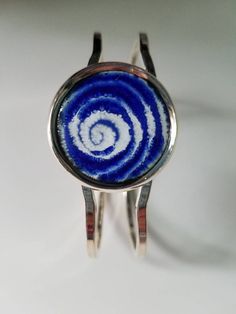 This unique bracelet is made with a hand designed and fired copper enameled disc set into a silver plated bangle. The disc is approximately 1 inch diameter and I've used cobalt blue enamel over white enamel. I've drawn a spiral design into the enamel. The bracelet fits all sizes. It is nickel and lead free. Unique Round Metal Cuff Bracelet, Blue Nickel-free Bangle Cuff Bracelet, Unique Blue Nickel-free Cuff Bracelet, Unique Blue Spiral-shaped Jewelry, Silver Enamel Cuff Bracelet As Gift, Blue Sterling Silver Round Cuff Bracelet, Adjustable Enamel Cuff Bracelet As Gift, Adjustable Enamel Cuff Bracelet For Gift, Blue Metal Jewelry