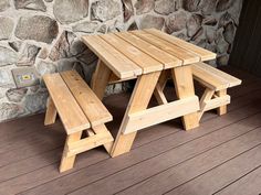 a wooden picnic table and two benches on a deck next to a wall with stone walls