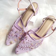 a pair of purple high heeled shoes sitting on top of a white bed sheet