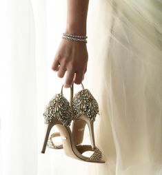 a woman's hand is holding a pair of high heeled shoes that are adorned with jewels