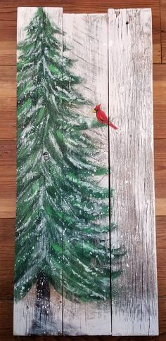 a red bird sitting on top of a wooden board next to a green pine tree