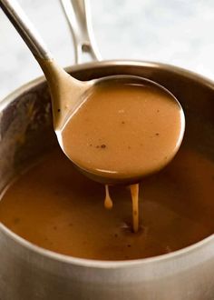 a spoon full of caramel sauce being poured into a pot with another ladle