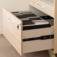 an open drawer with files and folders in it on a wooden floor next to a white wall