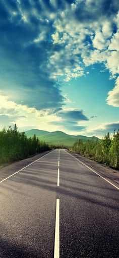 an empty road with trees on both sides under a blue sky filled with white clouds