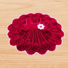 a crocheted doily with a flower on it sitting on a wooden surface