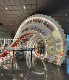 a library filled with lots of books next to a long table and book shelf on top of it