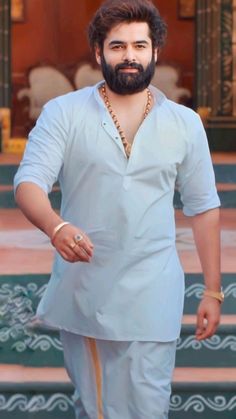 a man with a beard and white shirt is standing in front of steps wearing gold jewelry