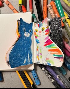 an open book with colored crayons and pencils around it, next to a drawing of a cat