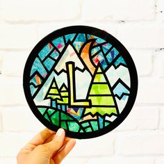 a hand holding up a stained glass piece with mountains in the background and trees on it