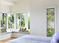 a bedroom with two windows and a bench in front of the window, along with pillows on the bed