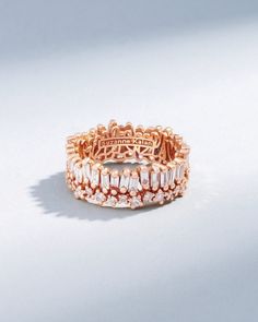 a rose gold ring with baguets and diamonds on the band, set against a white background