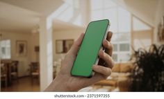 a hand holding a green cell phone in front of a living room and dining room