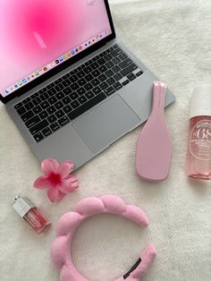 an open laptop computer sitting on top of a bed next to pink accessories and lipstick