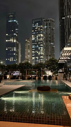 an empty swimming pool in the middle of a city with skyscrapers lit up at night