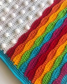 a crocheted blanket with multicolored stripes on the bottom and white dots at the top