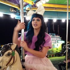 a woman in a pink dress riding on a merry go round with a white horse