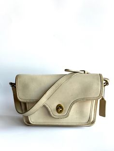 This vintage Coach Kent bag, dating back to 1993, is crafted in the classic bone color. The bag shows its age with some color wear at the corners and discoloration throughout, including on the strap. Despite this, the interior and the area under the flap remain very clean, highlighting its original vintage condition. A timeless piece for any Coach collector or vintage fashion enthusiast. Current style number 9916 Brass turnlock closure. Full-length outside back pocket. Full-length front gusseted pocket under leather-lined flap. Full-length inside zipper pocket. 48" Adjustable shoulder strap. 10" X 6" X 3" Butterscotch shown. Black, Bone, Bordeaux, Bottle Green, British Tan, Mahogany, Navy, Red, Stone. Classic Beige Rectangular Flap Bag, Classic Beige Shoulder Flap Bag, Classic Cream Flap Bag With Gold-tone Hardware, Classic Beige Bags With Brass Hardware, Classic White Flap Bag, Classic Beige Crossbody Satchel, Classic Beige Flap Bag For Formal Occasions, Classic Cream Flap Bag With Detachable Strap, Classic Cream Flap Bag For Everyday