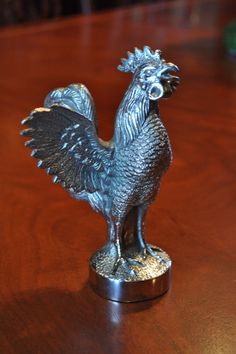 a silver rooster figurine sitting on top of a wooden table