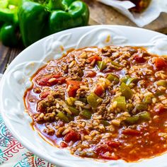 a white bowl filled with chili and beans on top of a wooden table next to green peppers