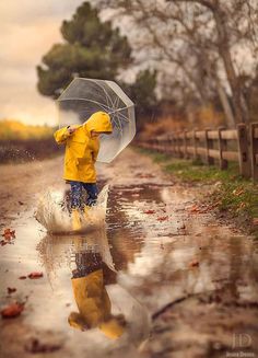 a person in yellow raincoat and blue jeans walking through water with an open umbrella