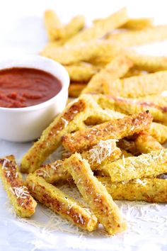 some cheesy bread sticks are next to a bowl of ketchup and dipping sauce