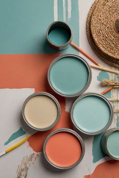 four paint cans with different colors and brushes next to each other on a painted surface