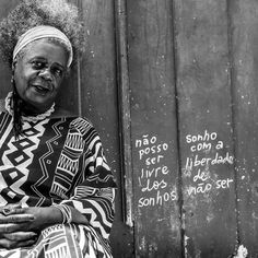 an old woman sitting in front of a wall with writing on it and wearing a head scarf