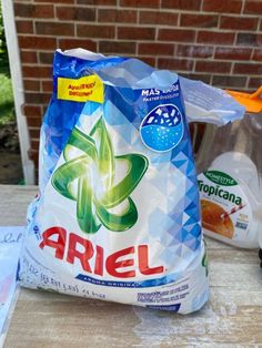 two bags of ariel detergent sitting on a table next to a bottle of liquid