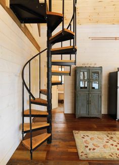 a spiral staircase in the middle of a room with wood flooring and white walls