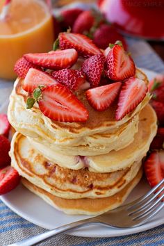 stack of pancakes with strawberries on top and orange juice in the backgroud