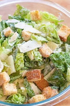 a salad with lettuce and croutons in a glass bowl on a wooden table