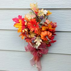 an arrangement of fall leaves and pumpkins hangs on the side of a house