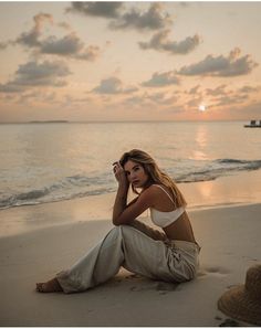 a woman sitting on top of a sandy beach next to the ocean