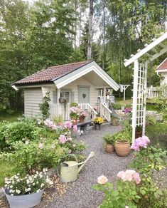 a garden shed with flowers and potted plants in the foreground, next to a gravel path