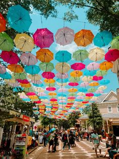 many colorful umbrellas are hanging from the ceiling in an open air area with people walking around