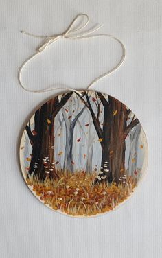 an ornament hanging from a string with trees in the woods painted on it