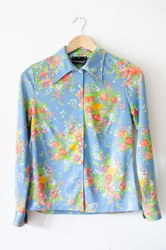 "1970's Floral Blouse with 70's style pointed collar. Stunning vintage blouse in the iconic 70's style. Light pastel blue fabric with floral print. The floral design is romantic, bouquet style. Arrangements of roses and wild flowers in light green and pastel pink hues. Slim fit, stretch shirt. Collared with a very pointy collar. Button up shirt with white plastic buttons. MEASUREMENTS:  Full length: 65 cm25,6\" Chest:          92 cm36,2 Waist:           84 cm33\" Shoulder seam to shoulder seam: Vintage Floral Pattern Shirt, Cheap Retro Long Sleeve Blouse, Cheap Long Sleeve Retro Blouse, Fitted Collared Shirt With Floral Print, Blue Shirt With Vintage Print For Spring, 1970s Style Retro Print Blouse For Spring, Retro Fitted Blouse For Spring, Fitted Vintage Print Collared Blouse, Retro Blue Floral Print Tops