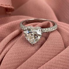 a heart shaped diamond ring sitting on top of a pink cloth