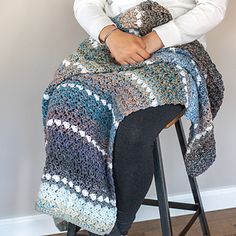 a woman sitting on a stool wearing a crocheted blanket