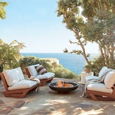 a fire pit sitting on top of a stone patio next to some chairs and trees