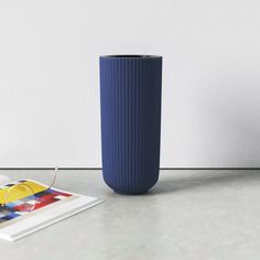 a blue vase sitting on top of a table next to a magazine and cup filled with liquid