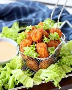 a basket filled with lettuce next to a bowl of dipping sauce on top of it